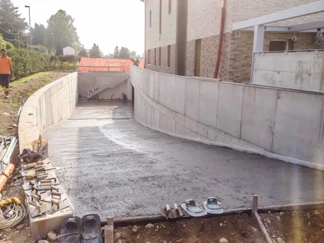Costruzione di una rampa in cemento fai da te, con attrezzi da lavoro e scarpe da cantiere in primo piano.