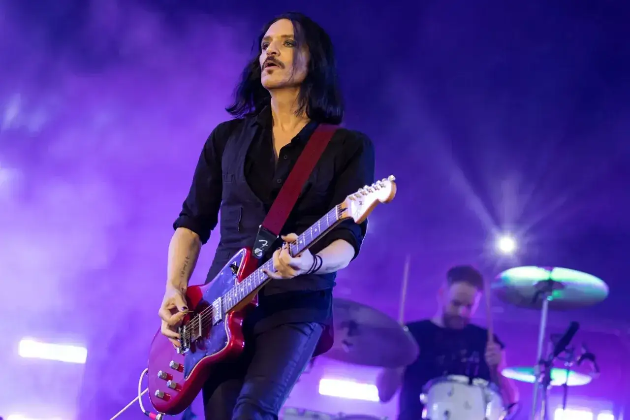 Brian Molko, le chanteur de Placebo, joue de la guitare rouge sur sc&egrave;ne, sous une lumi&egrave;re violette.