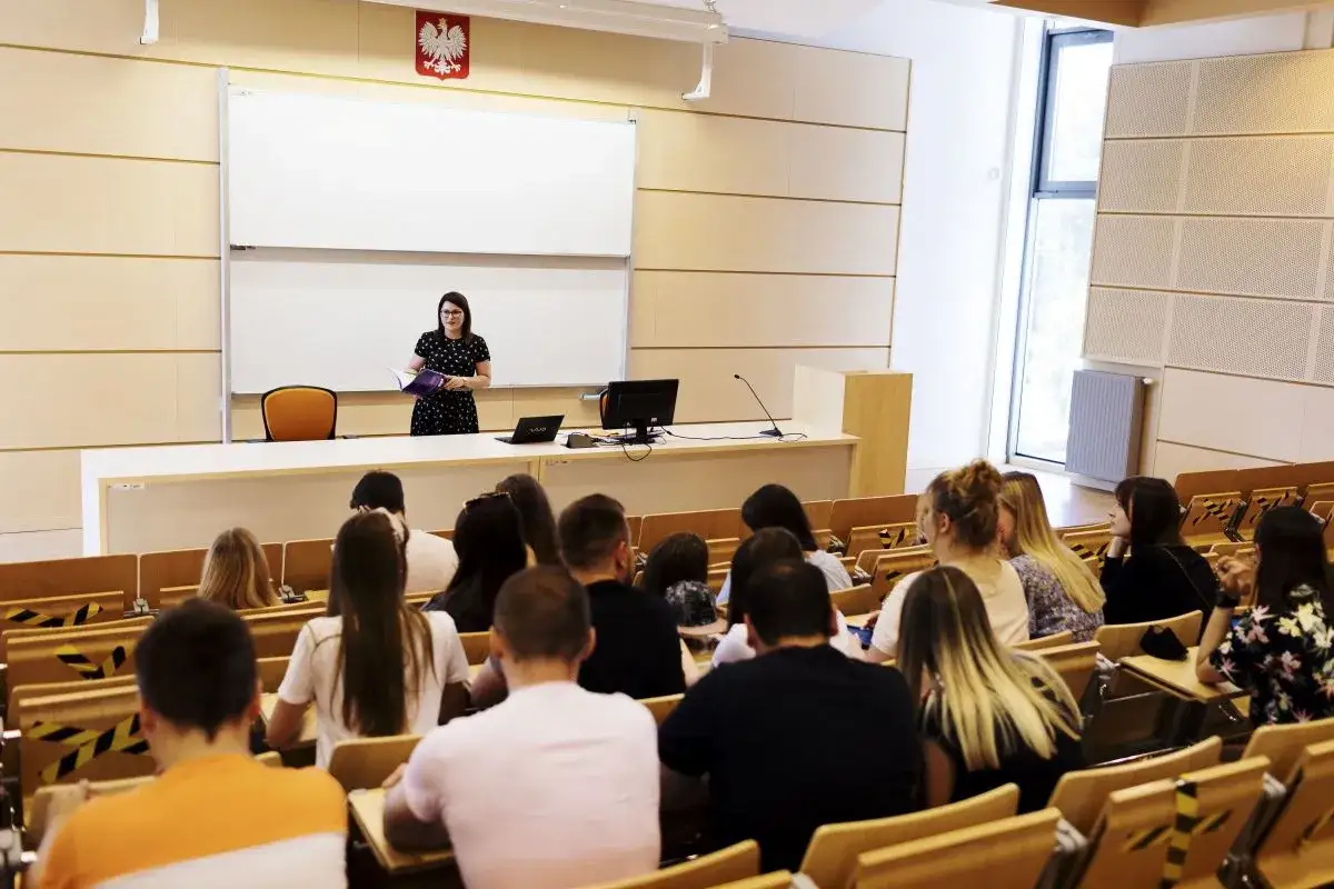 Wykładowczyni prowadzi zajęcia, odpowiadając na pytanie: studia podyplomowe co to? Studenci słuchają uważnie w sali wykładowej.