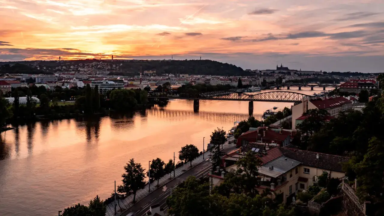 Zach&oacute;d słońca nad Wełtawą, widok z tarasu widokowego Czechy. Mosty i miasto w ciepłych barwach.