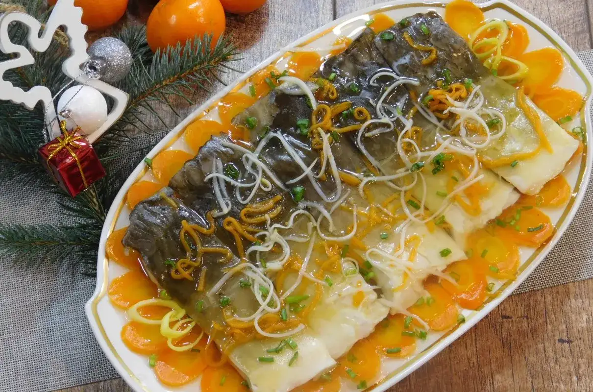Elegancki filet z karpia w galarecie, ozdobiony marchewką i szczypiorkiem, podany na świątecznym stole.
