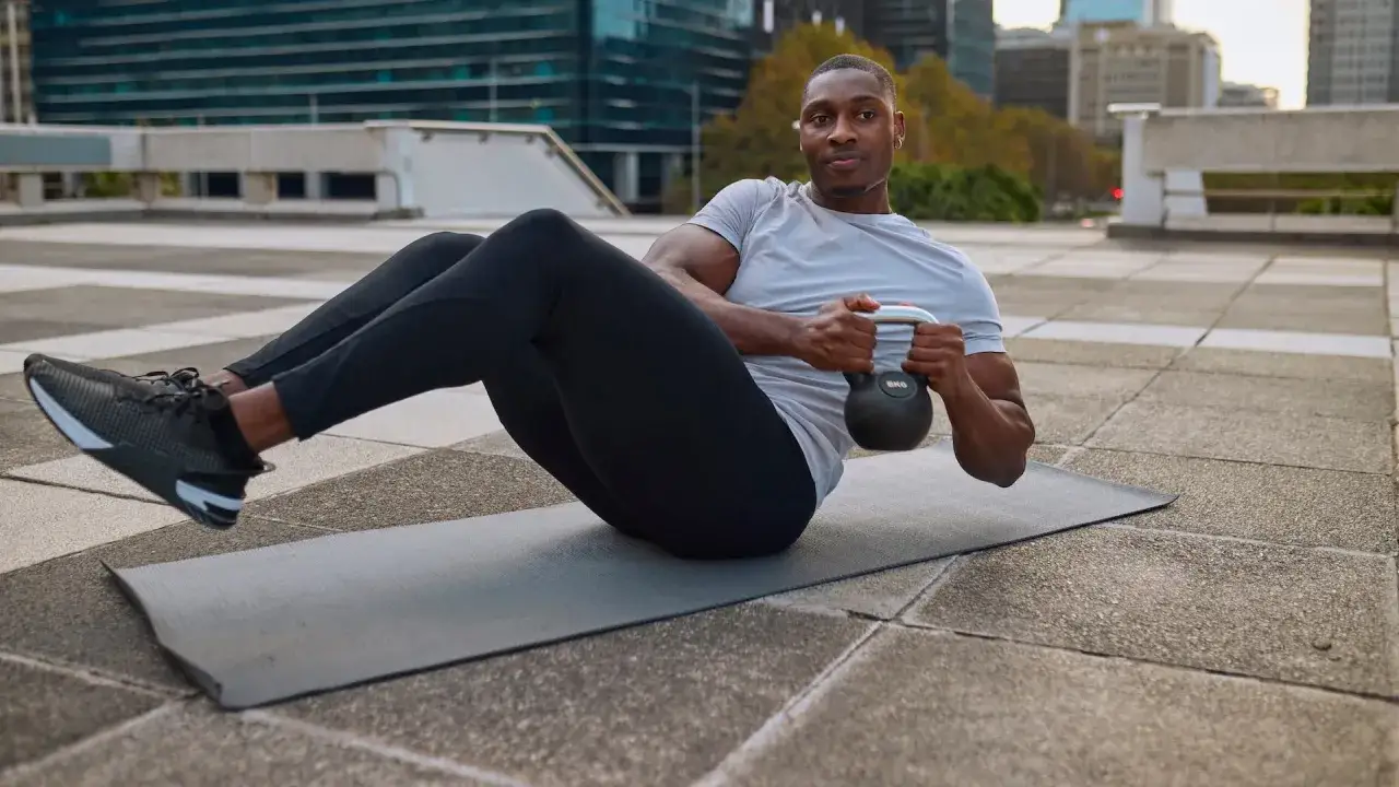 Mężczyzna wykonuje ćwiczenie russian twist z kettlebell, budując silne mięśnie brzucha. Efekty widoczne w wyrzeźbionej sylwetce.