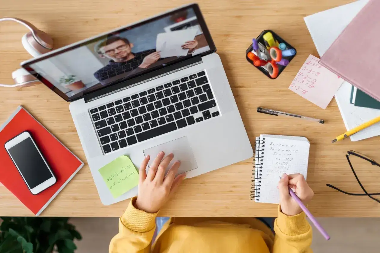 Dziecko uczy się zdalnie, korzystając z laptopa i notując w zeszycie. To przykład nauczania hybrydowego, gdzie technologia wspiera edukację.