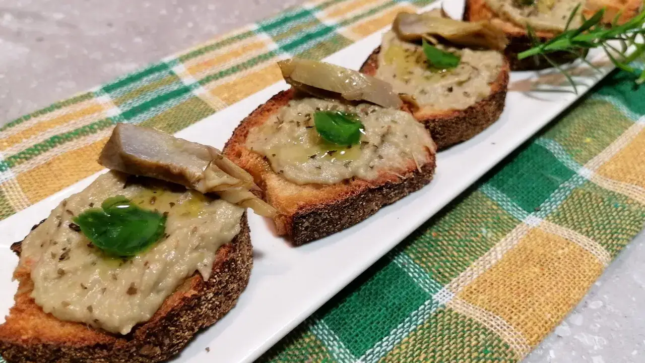Deliziosi crostini con crema di carciofi, guarniti con foglie di basilico fresco e un filo d'olio.