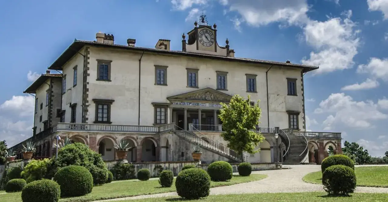 Villa Medicea di Poggio a Caiano, con il suo orologio sulla torre, circondata da un giardino curato e un cielo azzurro con nuvole bianche.