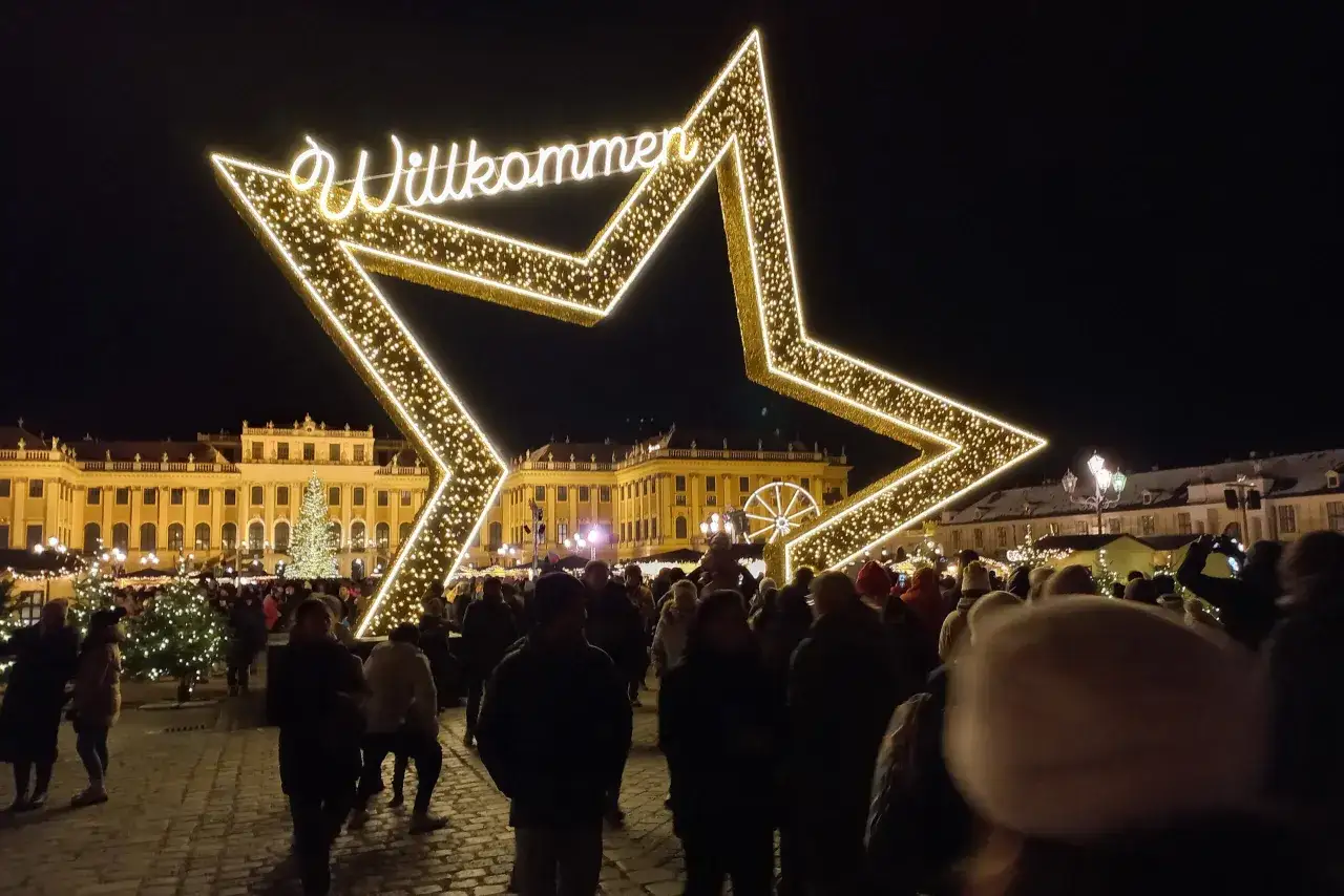 Tłum ludzi na jarmarku bożonarodzeniowym w Austrii, pod wielką, świecącą gwiazdą z napisem