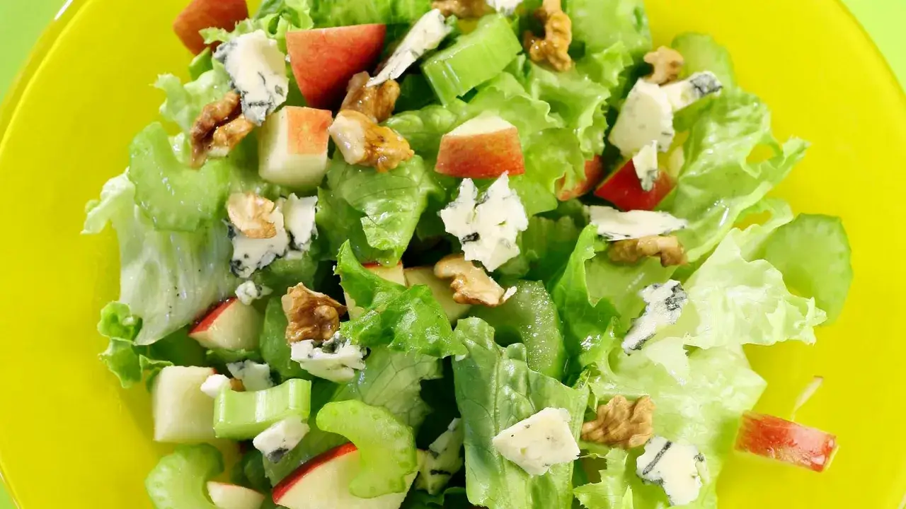 Ensalada de apio y manzana con queso azul y nueces, servida en un plato amarillo brillante.