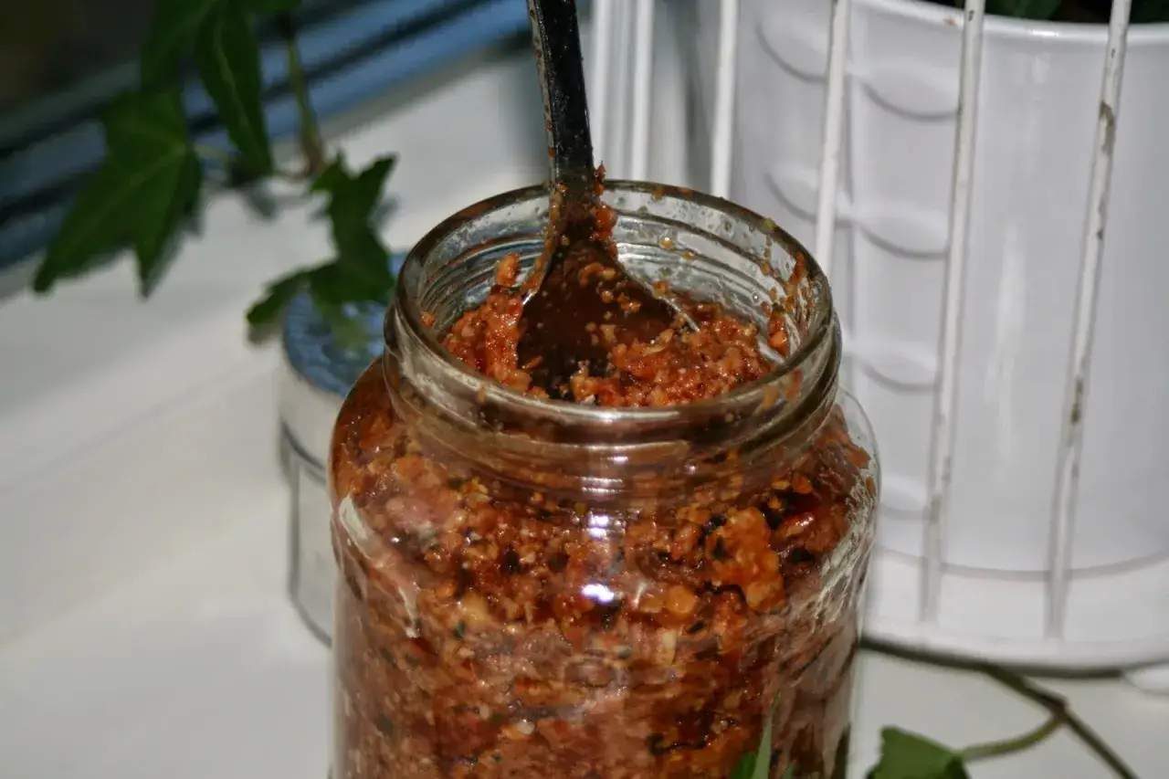 En burk med hemgjord egen pesto, redo att anv&auml;ndas. En sked sticker upp ur den smakrika blandningen.
