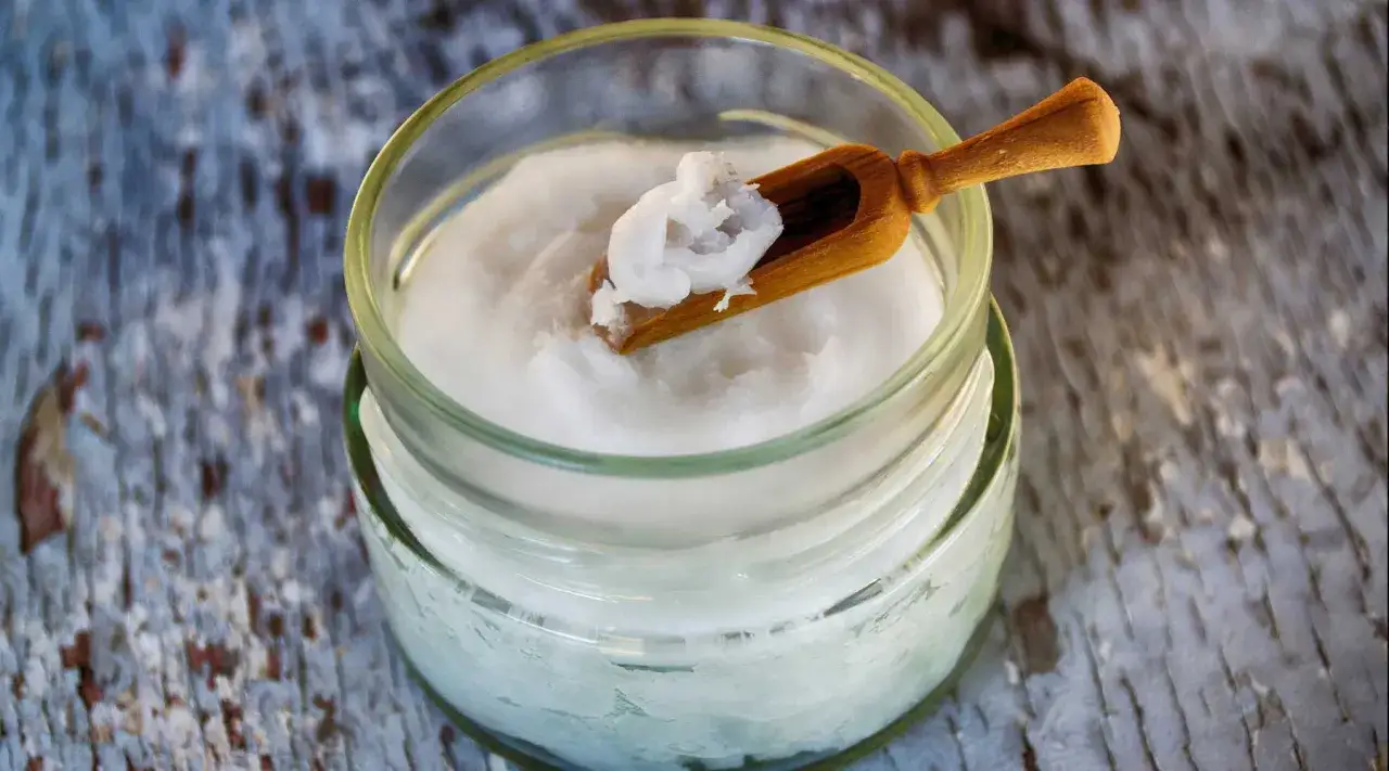 Un pot de noix de coco crémeuse, parfaite pour la peau, avec une petite cuillère en bois.