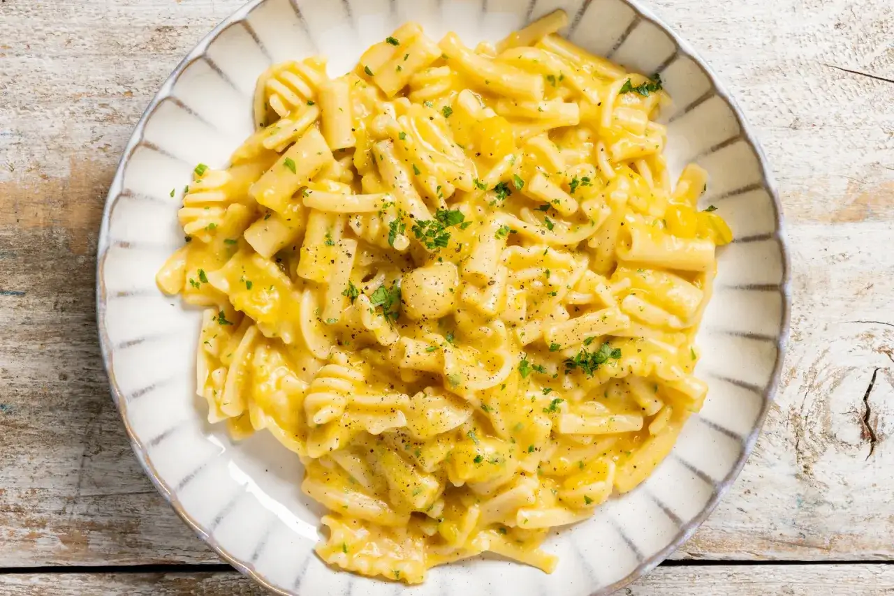 Piatto di pasta e zucca cremosa, condita con prezzemolo tritato e pepe nero, servita su un piatto bianco con bordo decorato.