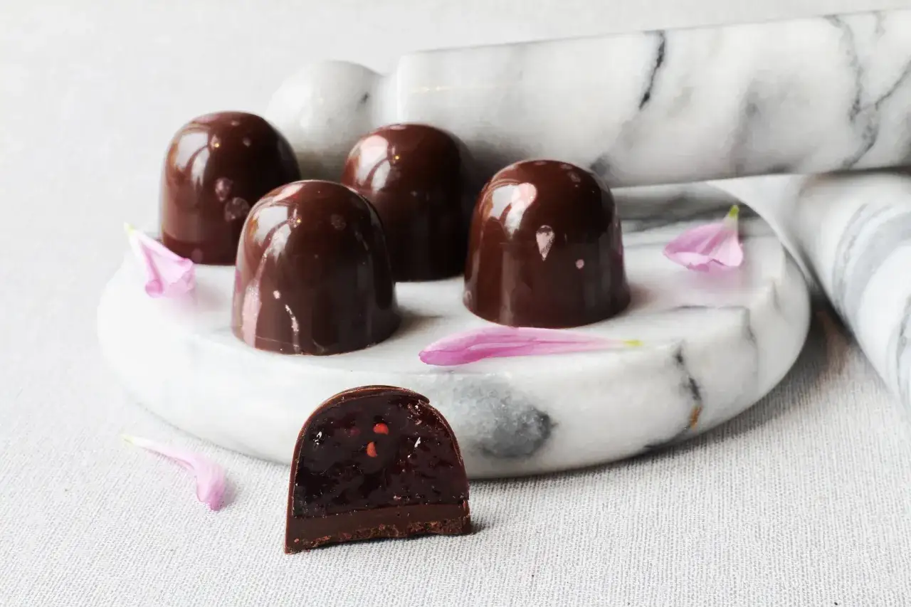 Chokladpraliner med en fyllning av bär, perfekta för ett ganache recept till praliner. Rosa blomblad ligger utspridda.