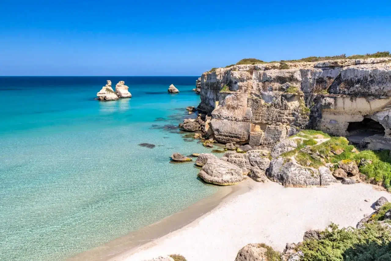 Scogliere calcaree e mare cristallino a Torre dell'Orso centro, con faraglioni che emergono dall'acqua turchese.
