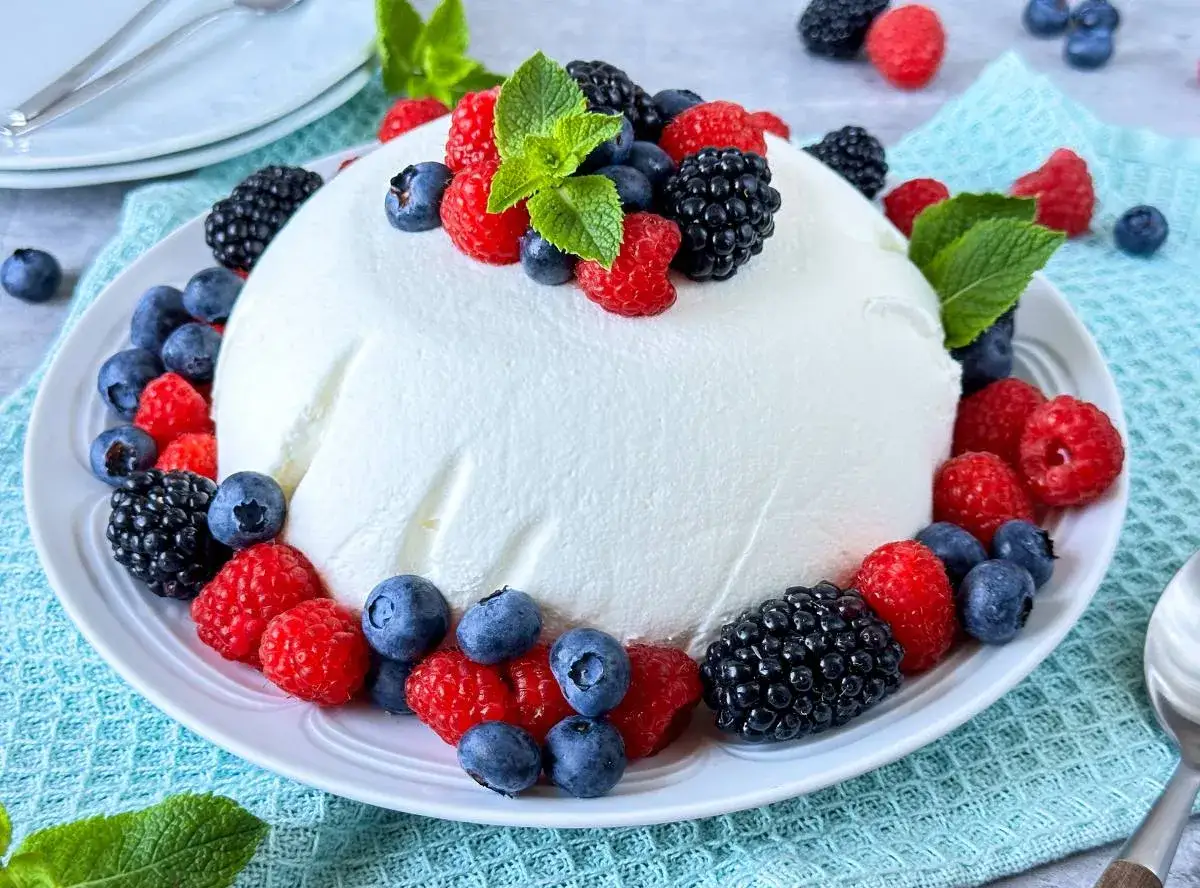 Ein erfrischendes Joghurtbomben-Rezept: Eine wei&szlig;e Joghurtmasse, verziert mit frischen Beeren wie Himbeeren, Blaubeeren und Brombeeren, garniert mit Minze.