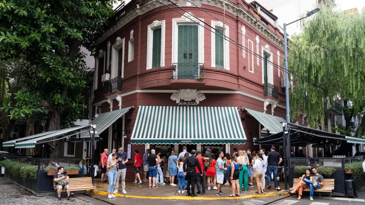 Gente esperando para entrar en la famosa parrilla Don Julio, con su toldo a rayas verdes y blancas.
