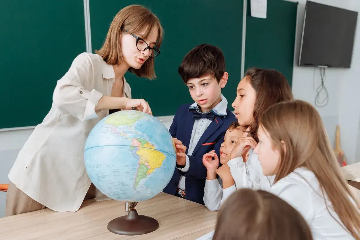 Nauczycielka z okularami pokazuje uczniom globus. To lekcja geografii, gdzie pragmatyzm co to jest, jest ważny w poznawaniu świata.