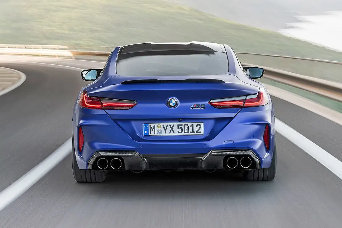 Der blaue BMW M850 Gran Coupé rast auf einer kurvigen Straße. Seine vier Auspuffrohre und das M8 Competition Emblem zeigen seine Leistung.