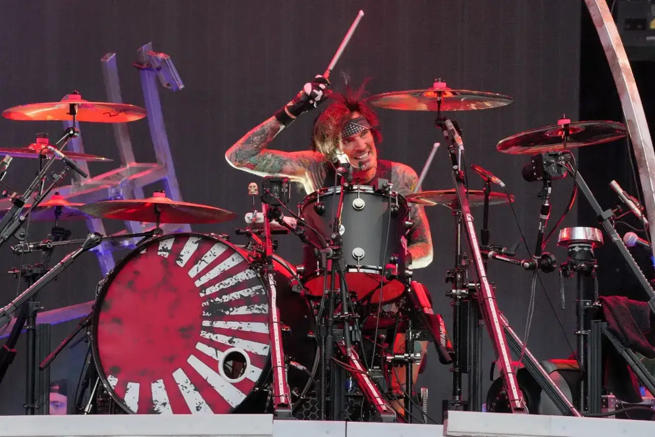 Tommy Lee w akcji za perkusją, z charakterystycznym uśmiechem i tatuażami, grając na scenie.
