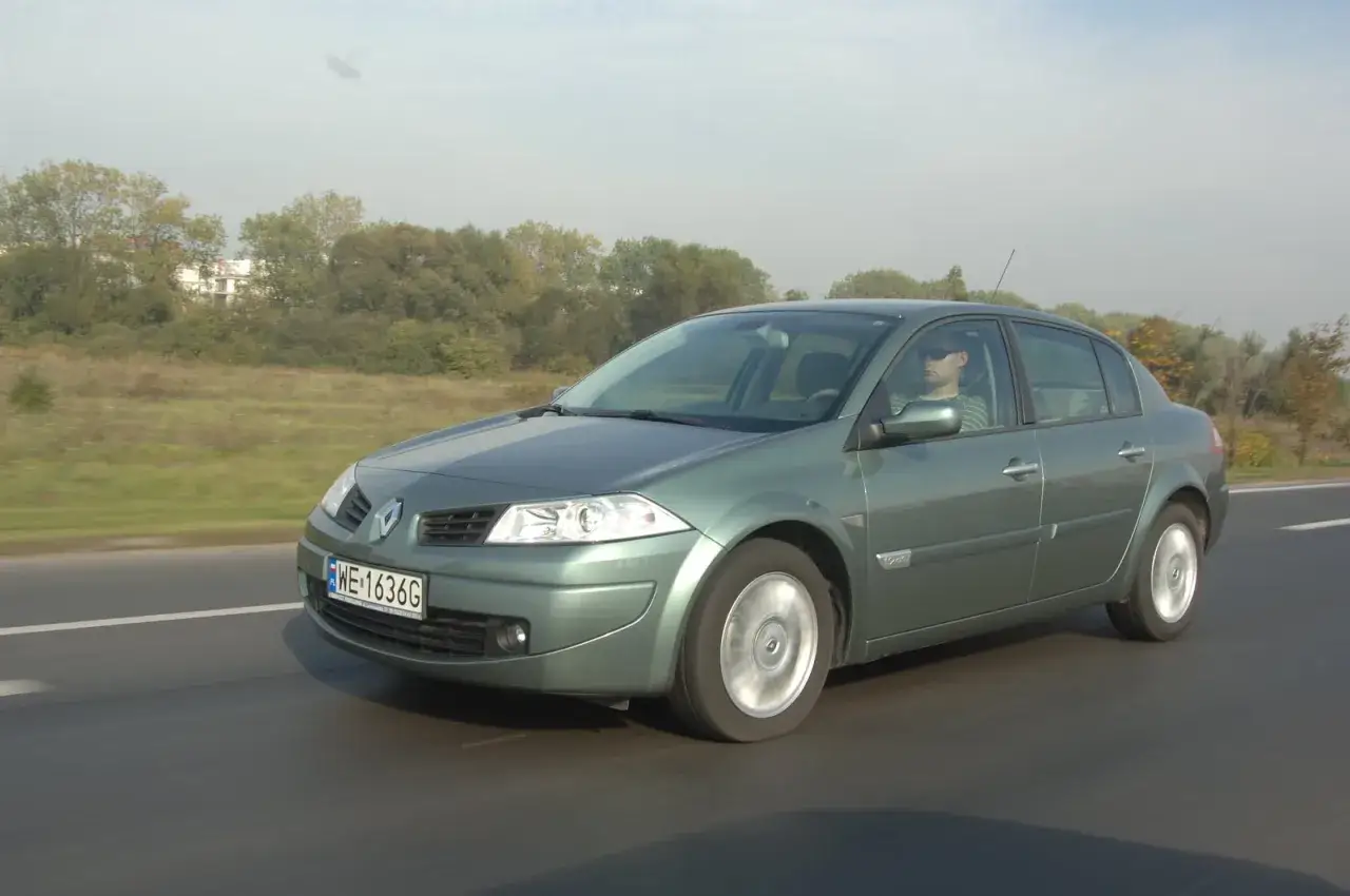 Zielony sedan Renault Megane 2 jedzie po drodze, za kierownicą mężczyzna w okularach przeciwsłonecznych.