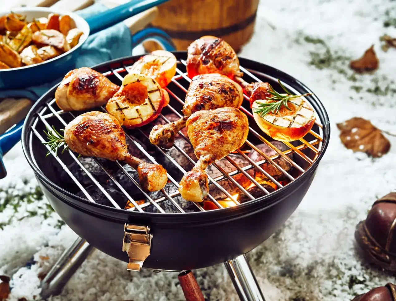 Poulet et pêches grillés sur un barbecue, avec des pommes de terre rôties à côté. Un barbecue hivernal inattendu, avec de la neige et des feuilles mortes.
