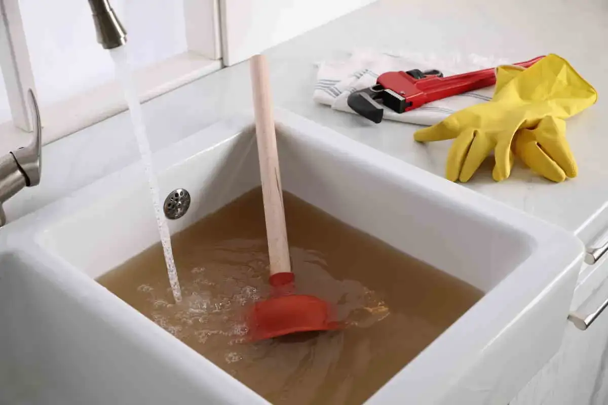Sturare la vasca da bagno in modo naturale: un water plunger rosso e guanti gialli pronti all'uso in una vasca piena d'acqua sporca.