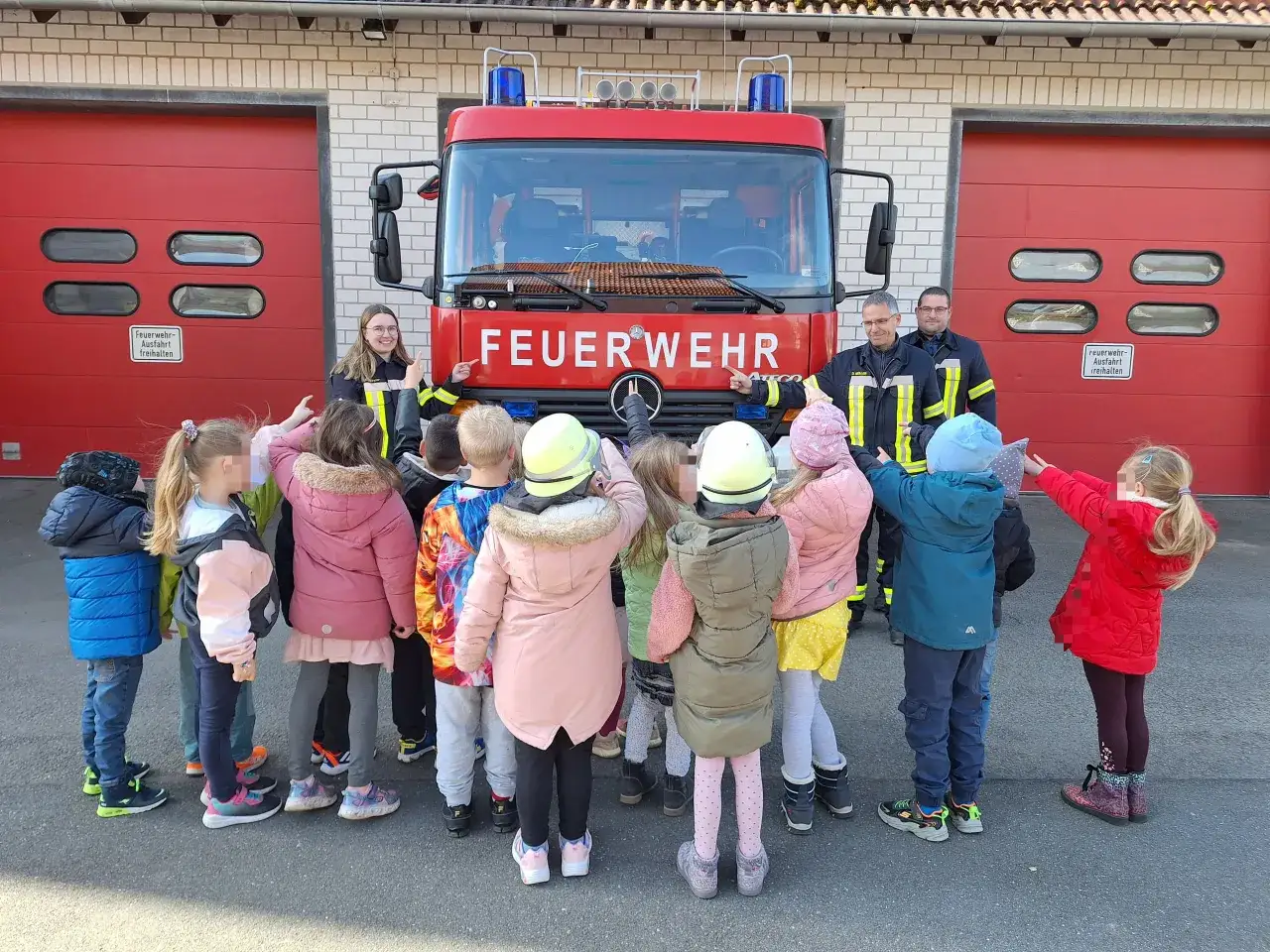 Kinder der Grundschule bestaunen ein Feuerwehrauto vor der Wache.