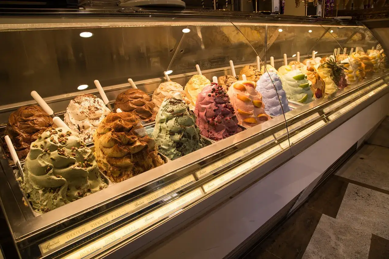 Un étalage de glaciers aux saveurs variées, comme un glacier romain, avec des parfums de pistache, chocolat et fruits.