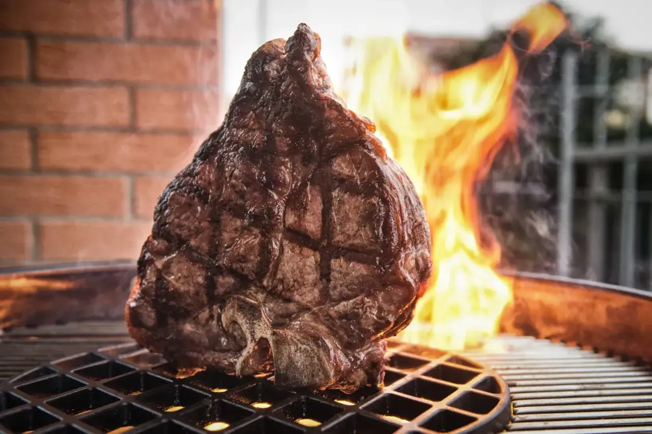 Una succulenta fiorentina alla griglia, con le fiamme che danzano sullo sfondo, promette un sapore indimenticabile.