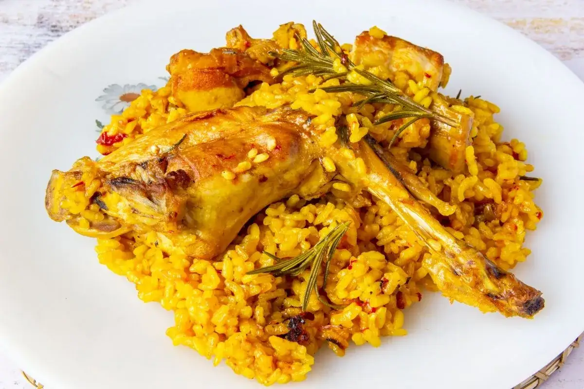 Deliciosa paella de conejo con arroz amarillo, trozos de carne dorada y ramitas de romero fresco.