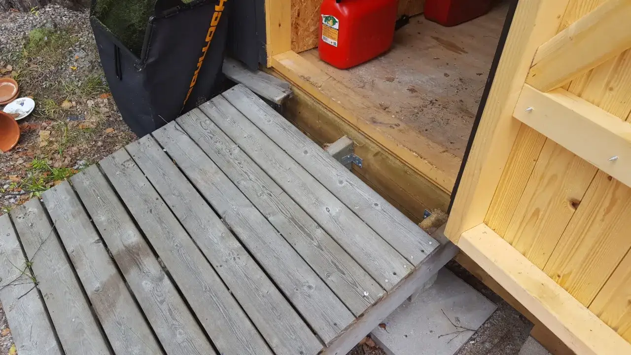 En träramp byggs till en trappa. En röd dunk och en grå gräsklipparpåse syns i bakgrunden.