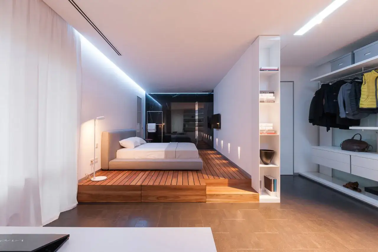 Moderne slaapkamer met verhoogd bed op houten platform, open kledingkast en minimalistische inrichting. Een perfecte ontspullen lijst voor een opgeruimd huis.