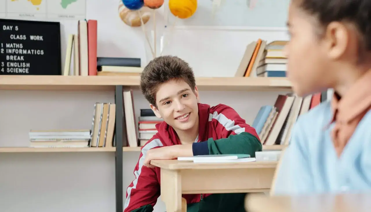 Ein Junge lächelt in der Schule, während er auf dem Tisch liegt. Hier gibt es keine pädagogisch sinnvollen Strafen, nur Lernfreude.