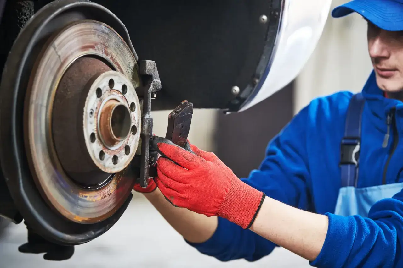 Mechaniker mit roten Handschuhen wechselt Bremsbeläge an einem Auto.