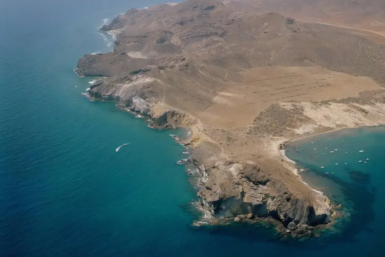 Vista aérea de la cala amarilla en Almería, con aguas turquesas y acantilados rocosos. Un barco navega cerca de la costa.
