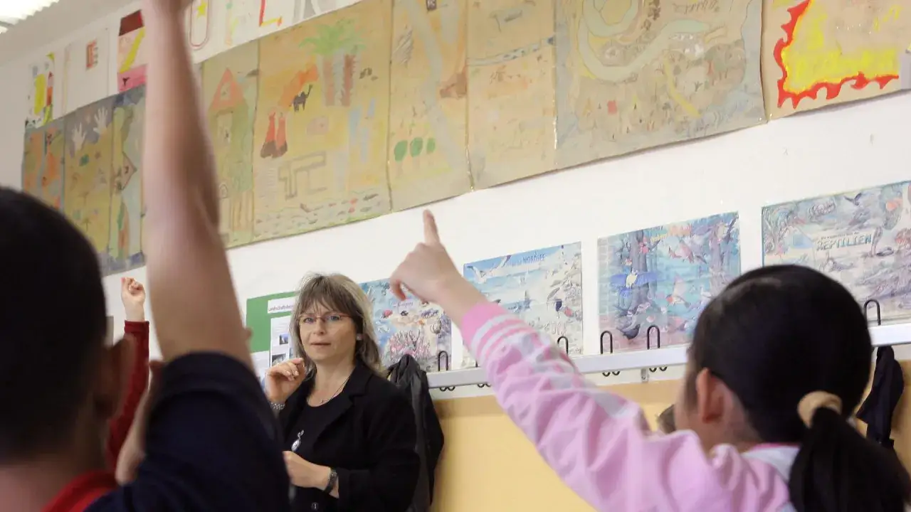 Lehrerin im Unterricht, Kinder melden sich. Ein Beispiel f&uuml;r Bildungsgerechtigkeit in Deutschland, wo jedes Kind z&auml;hlt.