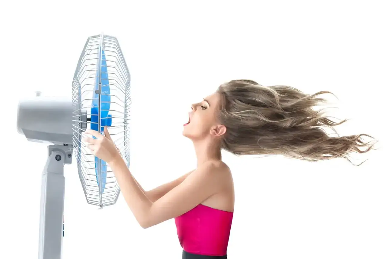 Mujer con cabello al viento frente a un ventilador, buscando trucos para no sudar por la cabeza en un día caluroso.