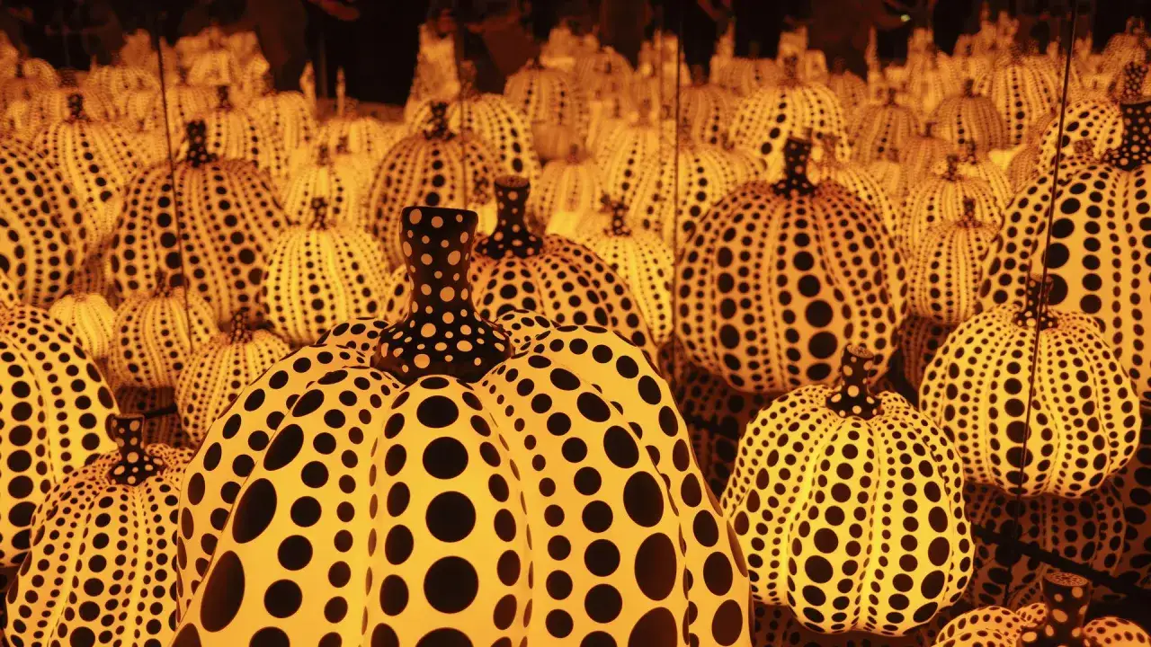 A room filled with glowing pumpkins featuring Yayoi Kusama patterns. The iconic polka dots cover the orange gourds, creating a mesmerizing, immersive art experience.