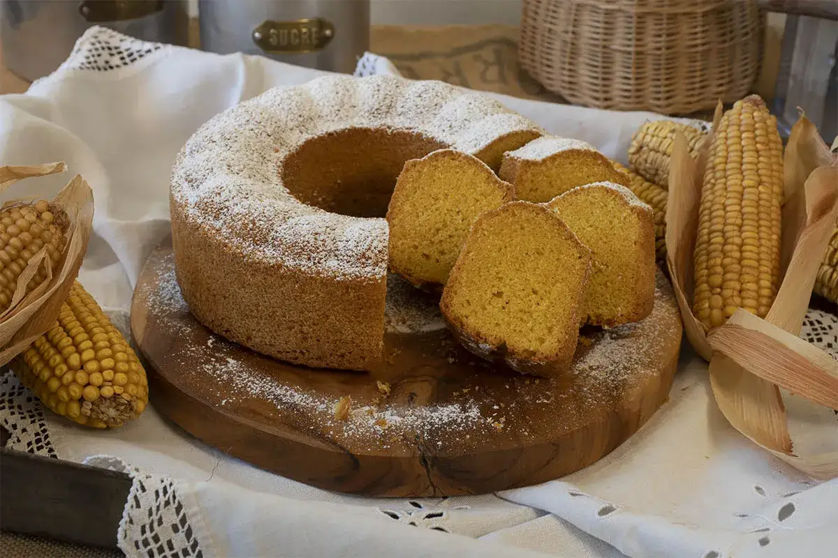 Torta de maiz esponjosa, espolvoreada con az&uacute;car glas, junto a mazorcas de ma&iacute;z y un cesto.