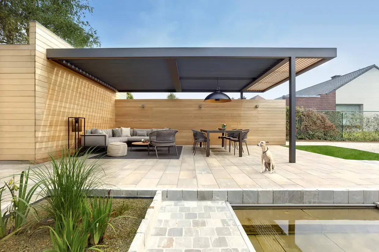 Une élégante terrasse en L avec salon et coin repas sous un auvent moderne. Un chien guette, profitant de la quiétude.