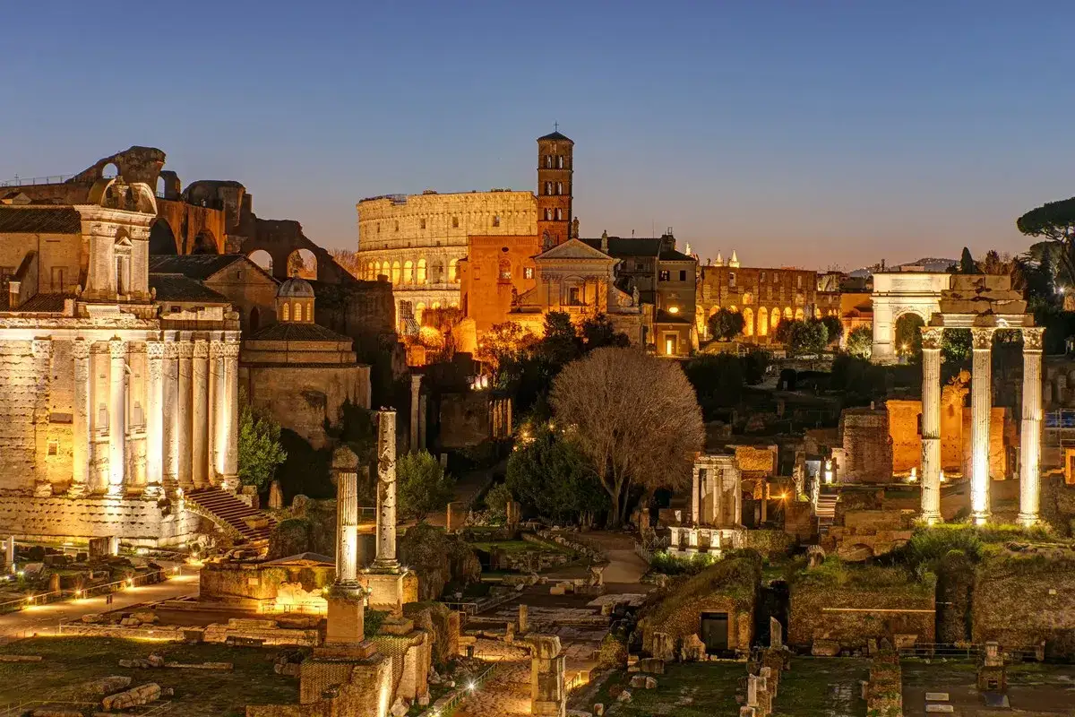 Antike Ruinen des Forum Romanum in Rom bei Nacht. Der Kolosseum und ein Triumphbogen sind beleuchtet. Ein wahrer tempel rom.