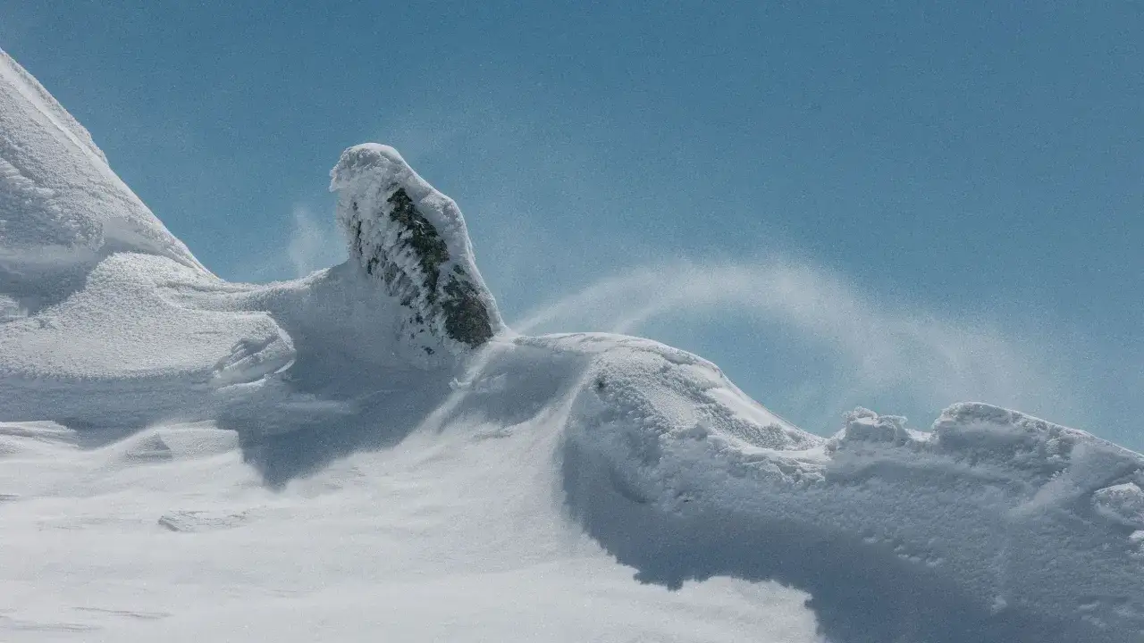 Paisaje invernal con nieve acumulada en rocas y viento que levanta el polvo blanco. Un lugar ideal para so&ntilde;ar con donde ver nieve en Madrid.