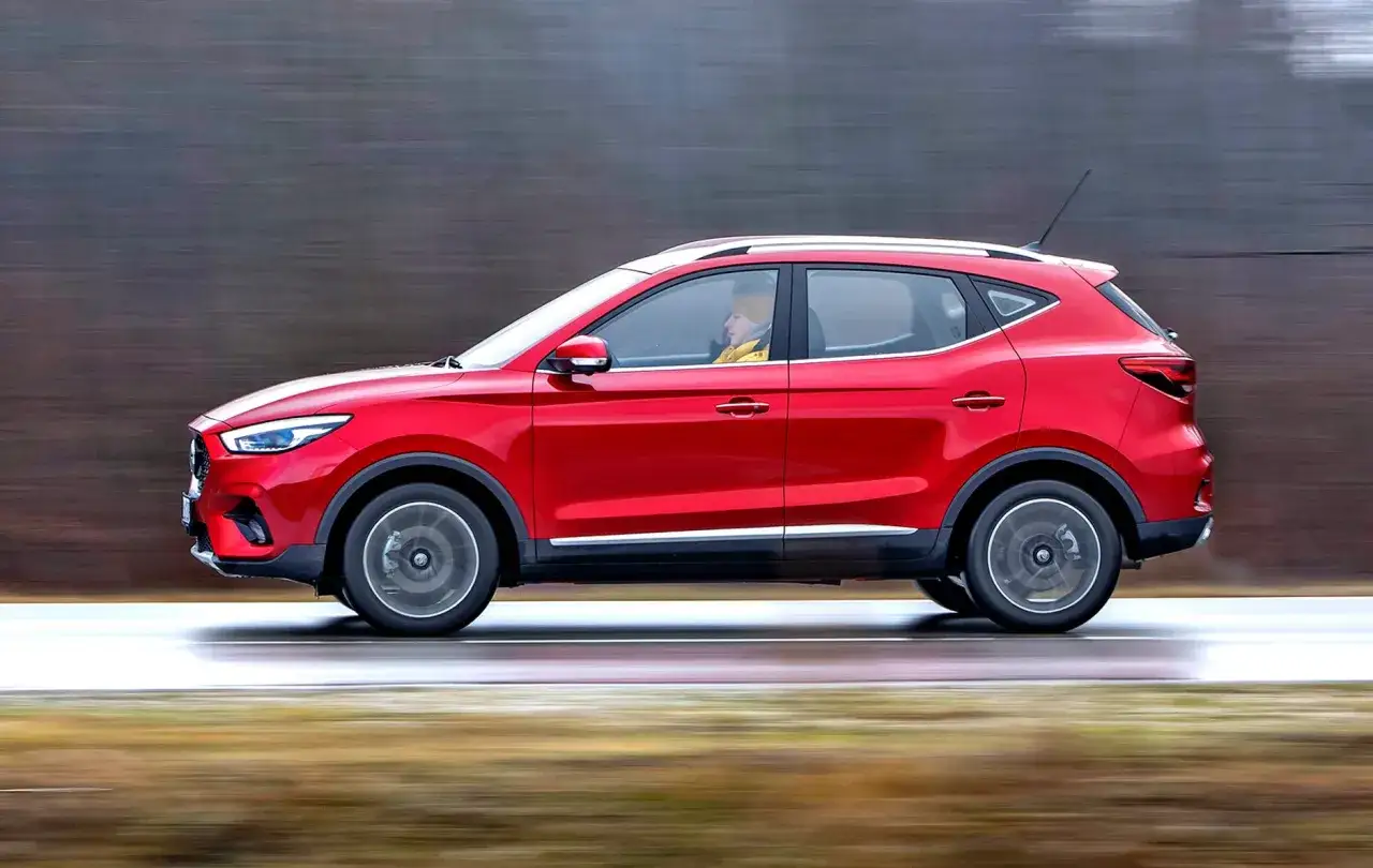 Czerwony MG ZS Classic pędzi po drodze, kierowca w żółtej kurtce.
