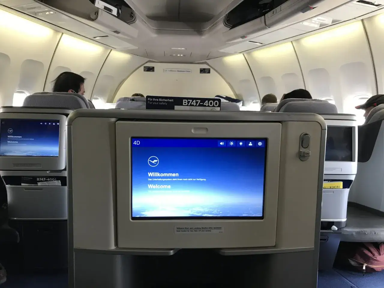 Lufthansa B747-400 kabin med passagerare. Underhållningssystemet visar