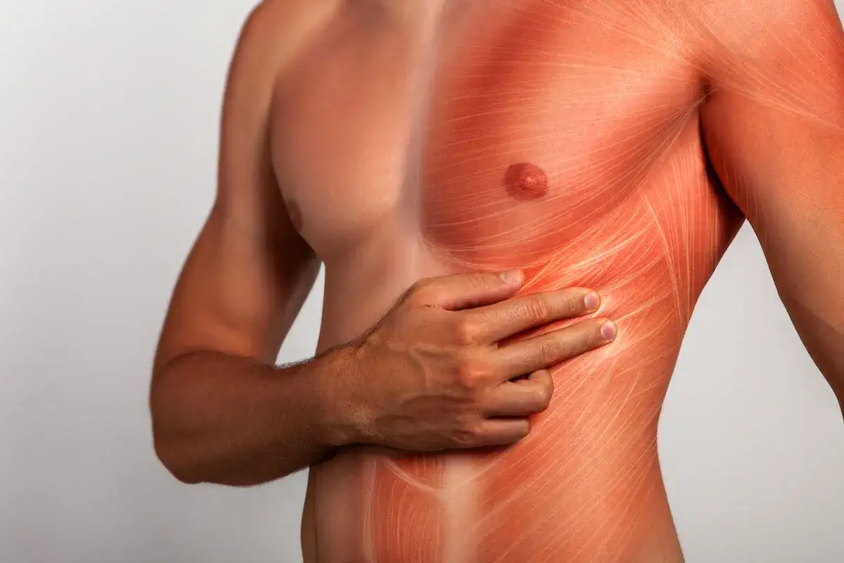 Hombre con la mano en el costado derecho, sintiendo pinchazos debajo de las costillas. La piel muestra un enrojecimiento y l&iacute;neas que simulan dolor muscular.