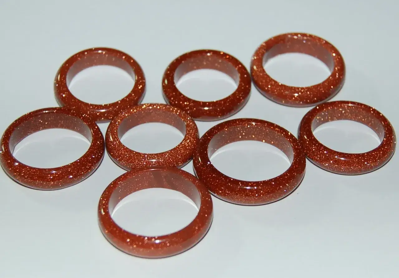 A collection of eight shimmering goldfluss stein rings, each a warm, coppery-brown with flecks of gold.