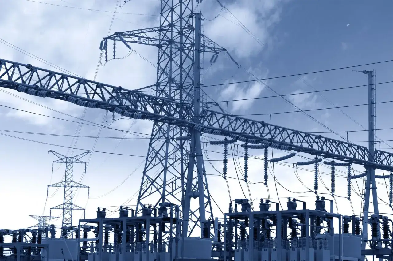 Ogromna stacja transformatorowa z wieżami energetycznymi i izolatorami pod błękitnym niebem.
