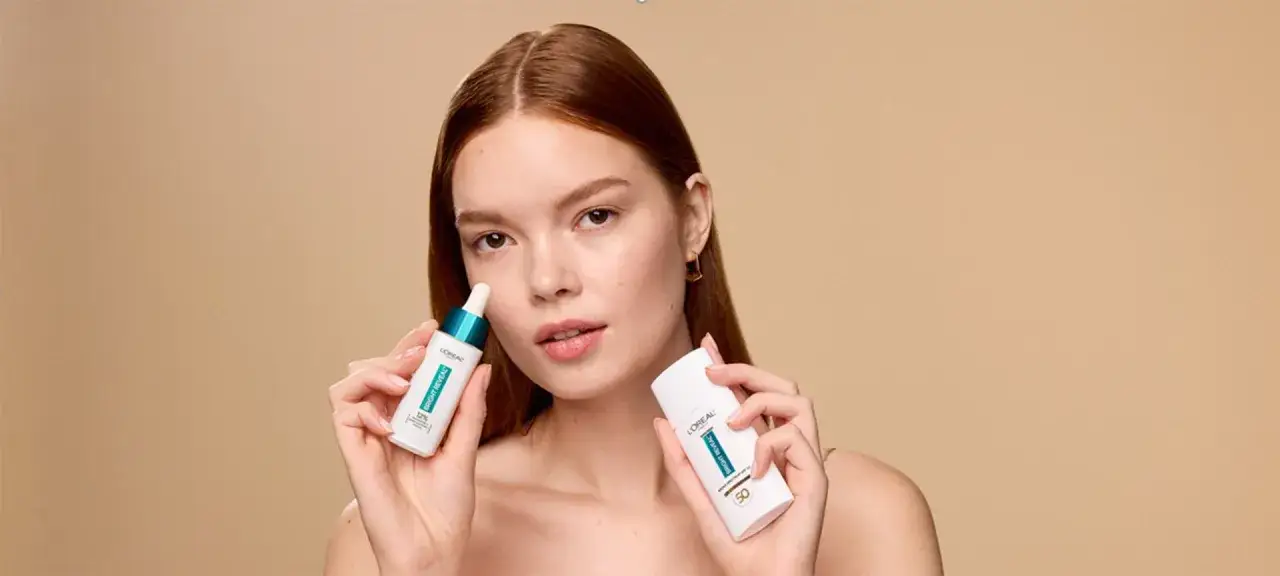 Rudowłosa kobieta prezentuje serum z niacynamidem i krem z filtrem SPF 50, chroniąc skórę przed słońcem.