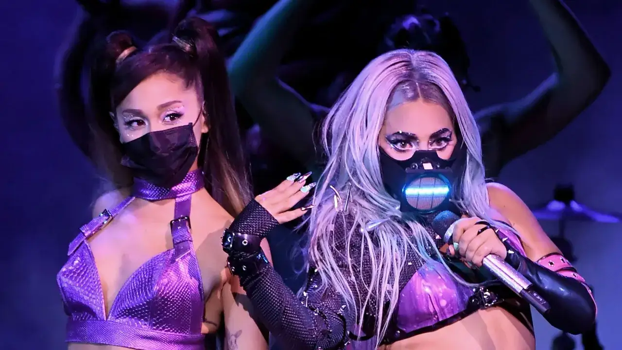 Ariana Grande i Lady Gaga w fioletowych strojach, z maskami na twarzach, gotowe na występ. Niech