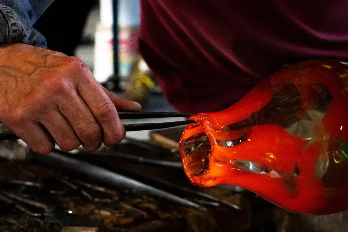Mano di vetraio lavora vetro incandescente con pinze. La temperatura fusione vetro Murano è alta, creando forme uniche.