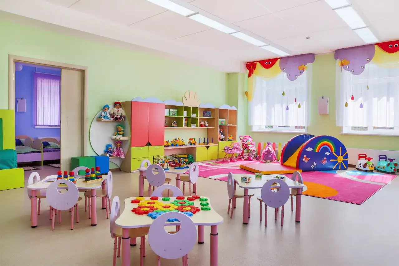 Ein fröhliches Kinder-Klassenzimmer einrichten mit bunten Tischen, Spielzeug und einer bunten Spielmatte.