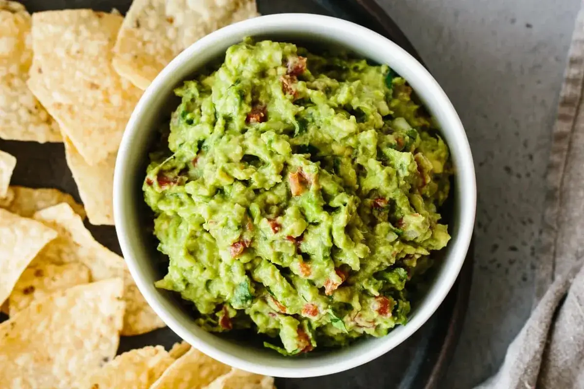 En skål med krämig guacamole, perfekt för ditt nästa guacamole recept, med tortillachips vid sidan om.